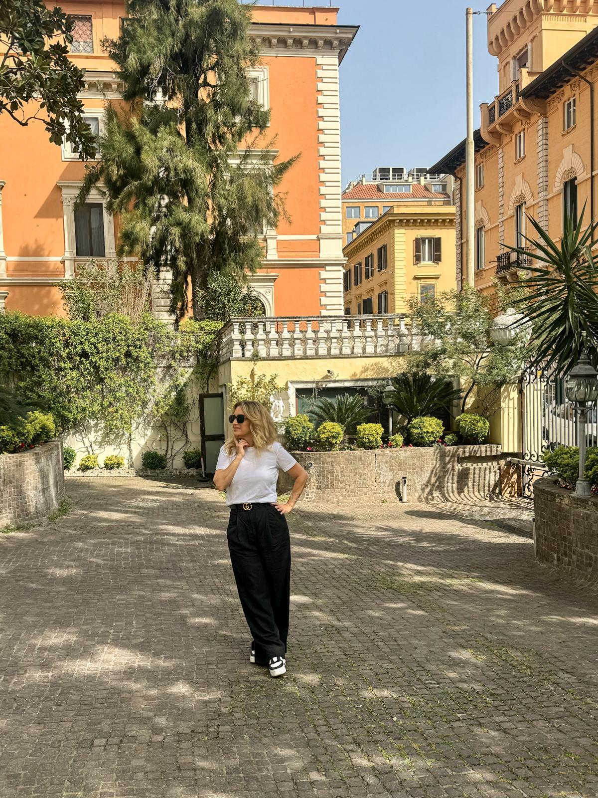A woman on a cobbled street lined with ochre buildings and greenery