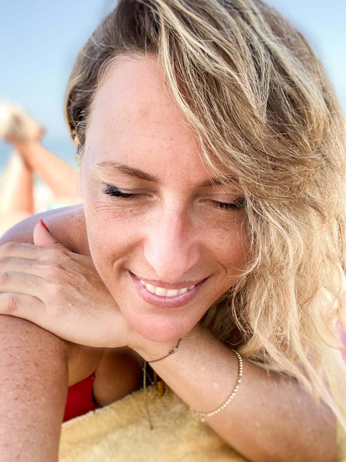 A close portrait of Elinor smiling in bright sunlight beside a pool