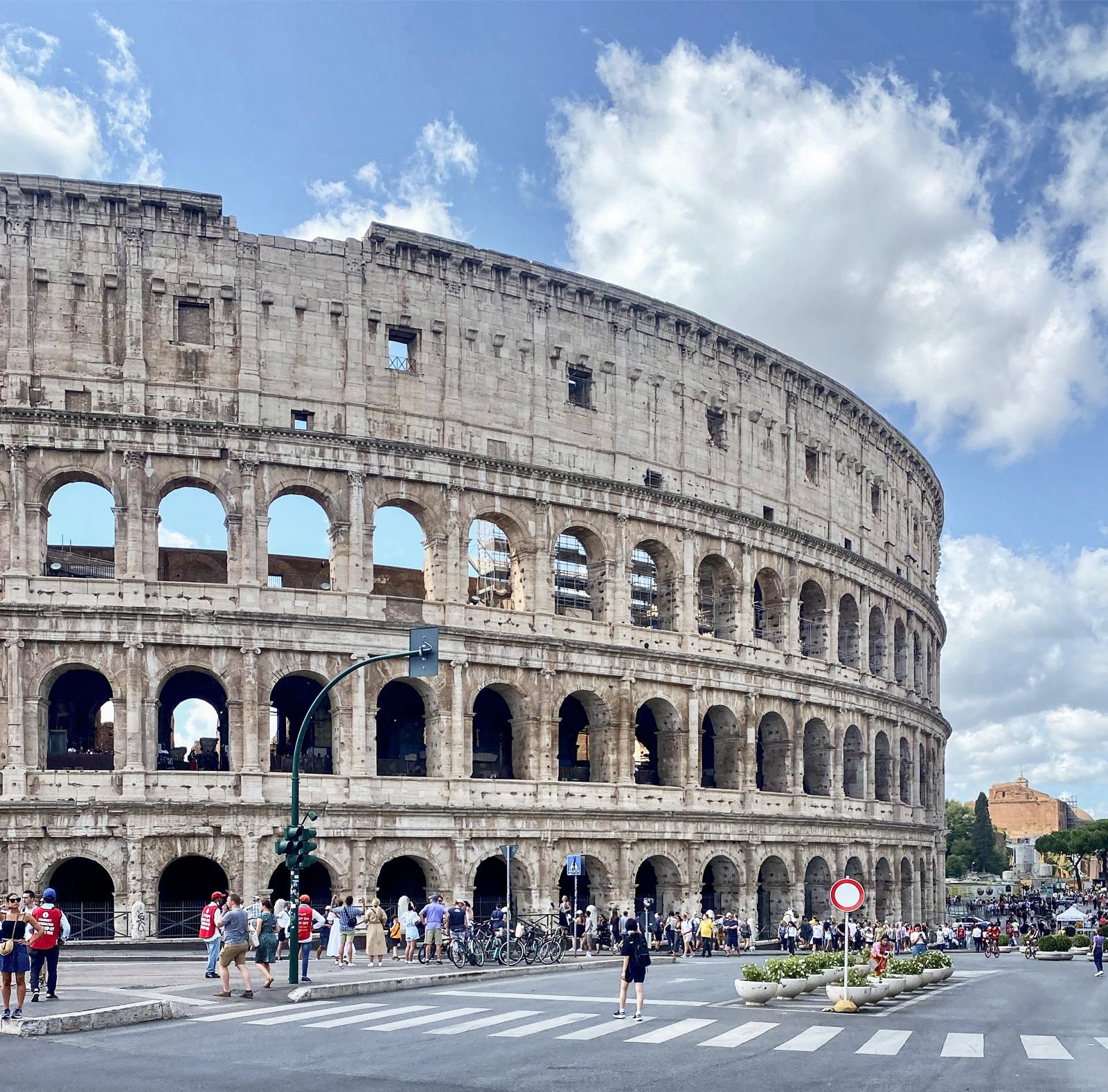 The Colosseum under a bright sky with crowds along the street