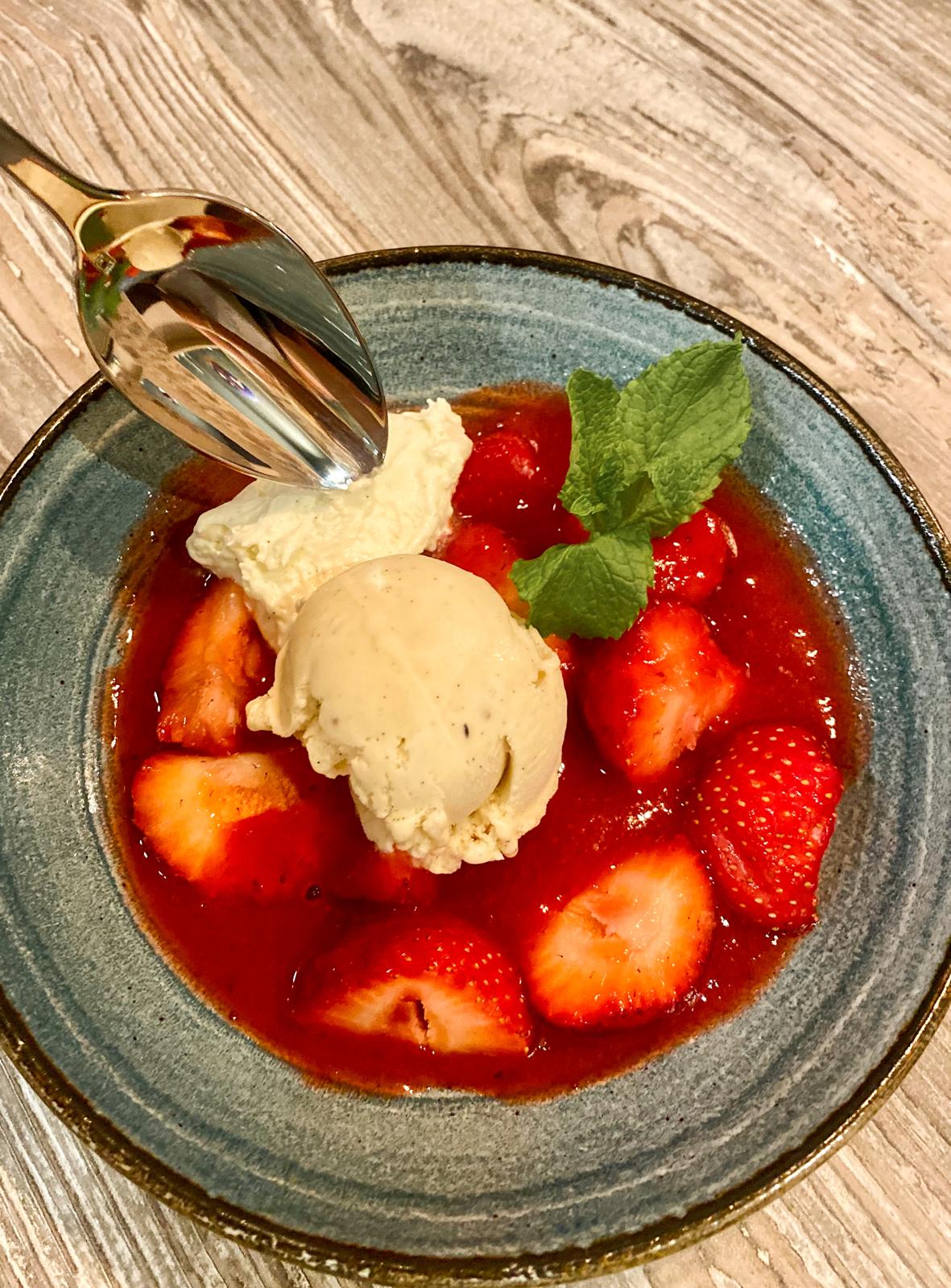 Strawberries in syrup topped with a scoop of gelato and mint, in a ceramic bowl