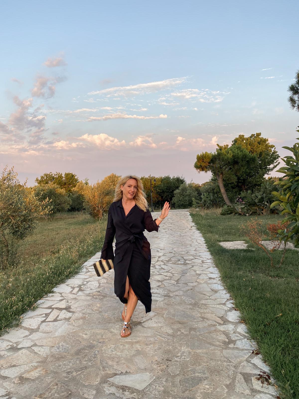 A woman in a black dress walking a stone garden path at dusk